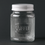 Glasburk i räfflat glas med vitt metallock och texten Coffee. Höjd 15,5 cm, diameter 12,5 cm. Praktisk och dekorativ kaffeförvaring med klassisk design.