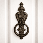 Dörrkläpp i gjutjärn i klassisk empirestil. Dekorativ och robust detalj för ytterdörr, monteras med skruv. Mått 24×8,5 cm.