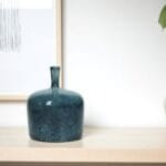 Elegant blå vas i glansig keramik med stilren, mjukt rundad form och smal hals; detaljen som ger designen sin karaktäristiska twist. Höjd 16 cm.