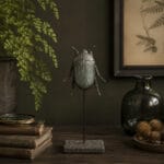 Dekorativ skalbagge på ställning med grönskimrande metallfinish. Ett detaljrikt ornament som passar fint i botaniska och rustika miljöer.