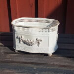 Rektangulär plåtkruka med genombruten kant, kulfötter och blomstergirlang. Mått 22x16x14 cm (lxbxh).