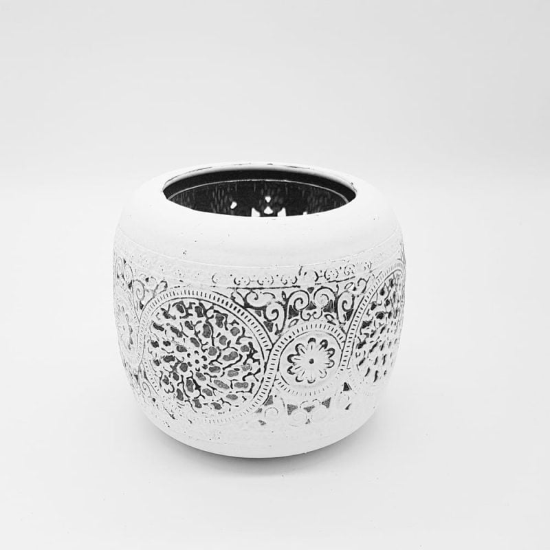 Ljuslykta i vit metall med genombruten dekor. Försedd med glascylinder för placering av värmeljus. Diameter 11 cm, höjd 9,5 cm.