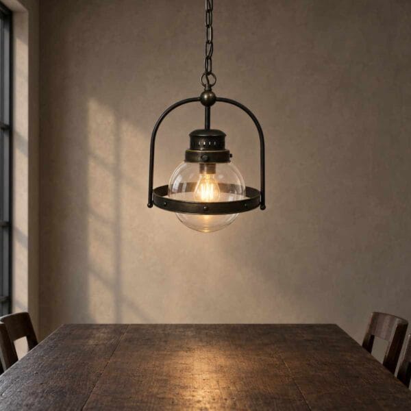 Taklampa Brooklyn i mörk metall och klart glas med en tänd ljuskälla över ett mörkt träbord.