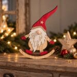 Dekorativ jultomte i trä på gungande medar med röd luva och guldglitter som ger lite extra julkänsla. En charmig juldekoration 27,5 cm hög.