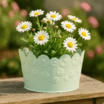 Blomkrukan Daisy kommer med somrig charm. Rund kruka i plåt med reliefmönster av prästkragar runt om. Lekfull spetskant och blommig design. Dia 18,5 cm.