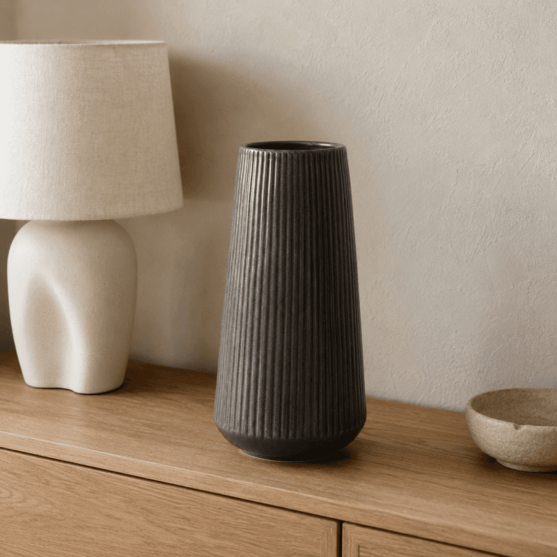 Varmgrå vas i keramik med hög avsmalnande form och vertikala räfflor. En stilren inredningsdetalj med ett grafiskt uttryck. Ø 15 cm H 30 cm.