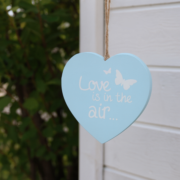 En söt hängande dekoration i form av ett hjärta, tillverkat i ljusblått trä med texten "Love is in the air..." och små fjärilar. Hängs enkelt upp med det medföljande snöret i jute. Perfekt som en liten romantisk detalj i hemmet, passar även fint som gåva till någon du tycker om. Mått 15,5x15,5x1 cm (lxhxd).