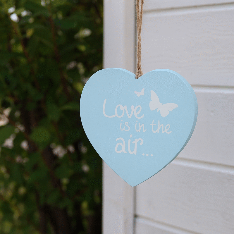 En söt hängande dekoration i form av ett hjärta, tillverkat i ljusblått trä med texten "Love is in the air..." och små fjärilar. Hängs enkelt upp med det medföljande snöret i jute. Perfekt som en liten romantisk detalj i hemmet, passar även fint som gåva till någon du tycker om. Mått 15,5x15,5x1 cm (lxhxd).