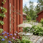 Väggmonterat fågelbad i antikbehandlad metall med ett skyddande paraply för skugga. Fungerar även som matstation på vintern. Enkel montering.