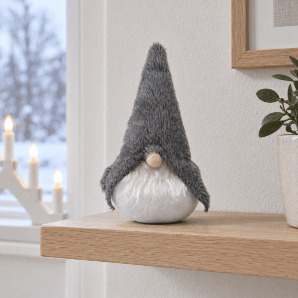 Grå textiltomte 13,5 cm på vägghylla med adventsljusstake i fönstret