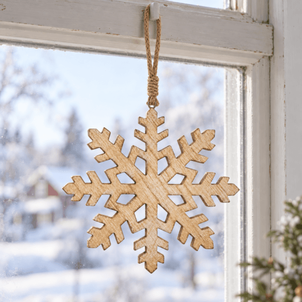 Hängdekoration i trä formad som en snöflinga hängande i ett ljust vinterfönster