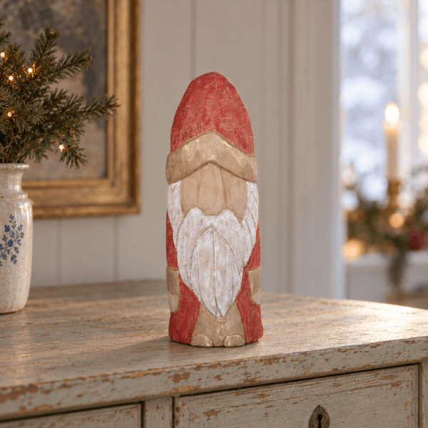 Jultomte i bemålat trä med röd luva och ljust skägg i varm julmiljö