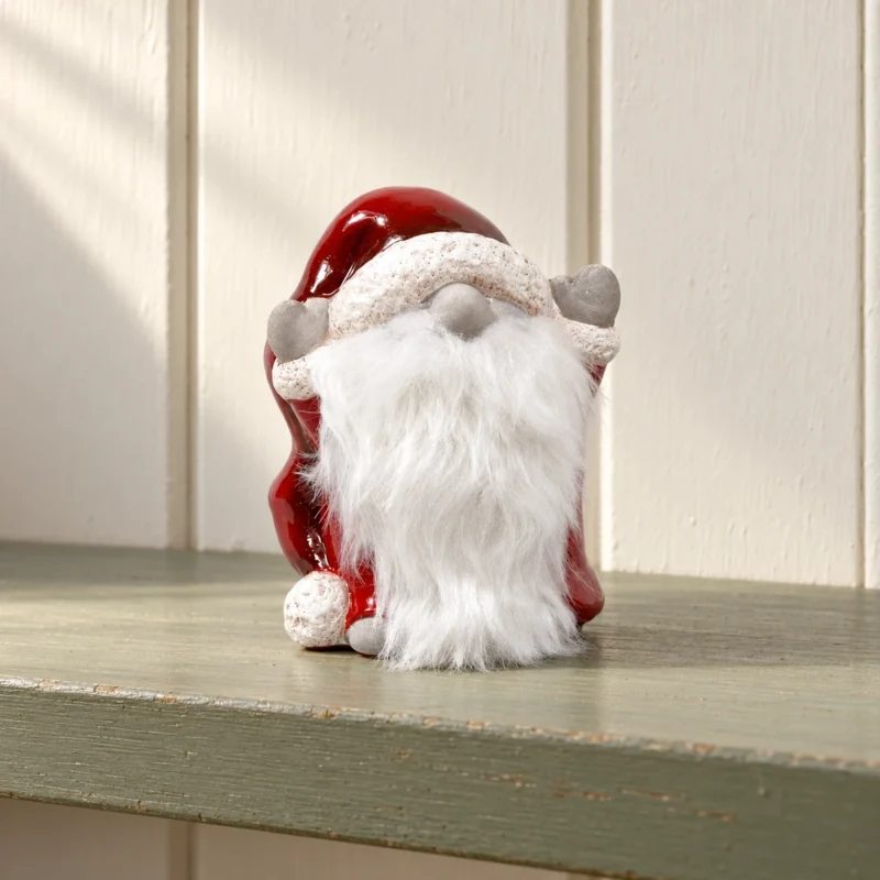 Tomte med röd luva på grön hylla Tomte med röd luva, grå vantar och vitt skägg på en dovt grön trähylla.