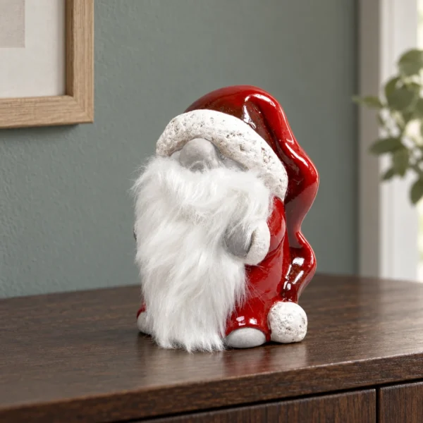 Röd tomte med böjd luva och långt vitt skägg stående på en mörk träskänk