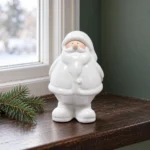 Vit tomte i keramik på en fönsterbräda i trä med en liten grankvist bredvid