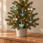 Sex små hjärtan i grönt och guld hänger i en liten julgran med varmvit ljusslinga.