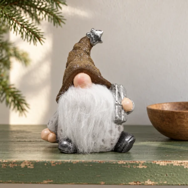 Tomte med brun mössa, vitt skägg och silverfärgat paket på en grönmålad hylla intill en liten träskål.