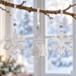 Två olika vita snöflingor och en gran i trä hänger från en gren framför ett fönster i vinterljus.