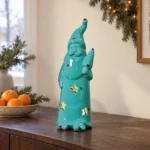 Turkos ljuslykta i form av en tomte på en mörk träskänk med ett fat apelsiner bredvid