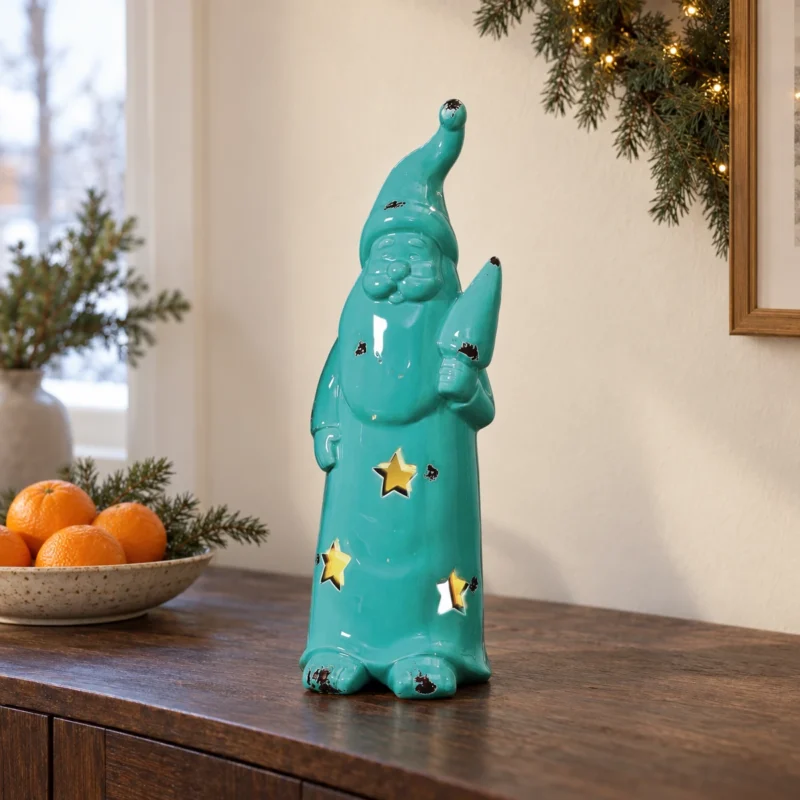 Turkos keramiktomte 42 cm på träskänk Turkos ljuslykta i form av en tomte på en mörk träskänk med ett fat apelsiner bredvid