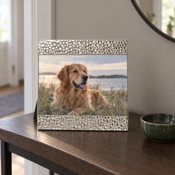 Silverfärgad fotoram med strukturerad dekor och ett hundfotografi på en mörk träkonsol intill en grön keramikskål.