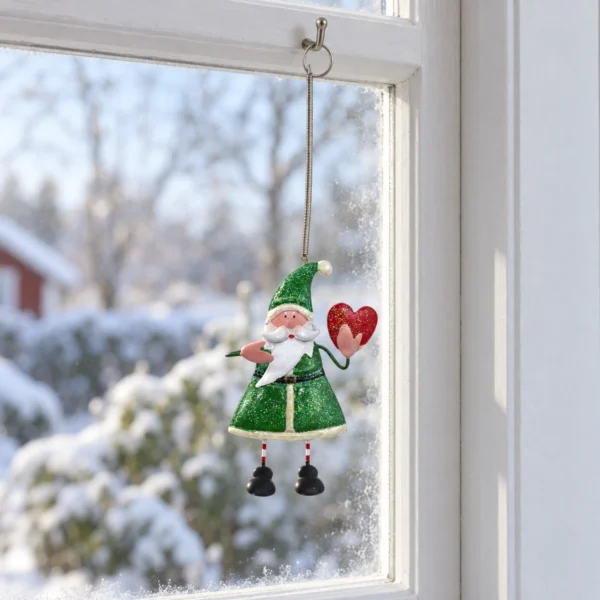 Grön glittrande tomte med rött hjärta och dinglande ben hängande i sin metallfjäder i ett vitt träfönster.