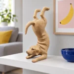 Beige yogahund på en vit hylla med en inramad bananbild och en koboltblå keramikskål.