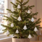 Tolv vita granformade hängdekorationer i plåt med bruna snören på en levande bordsgran.