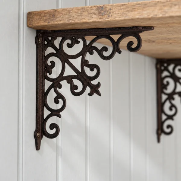 Mörk ornamenterad konsol i gjutjärn under ett trähyllplan mot ljust gråmålad pärlspont.