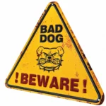 Trekantig gul plåtskylt med bulldogg och texten BAD DOG och BEWARE mot vit bakgrund.